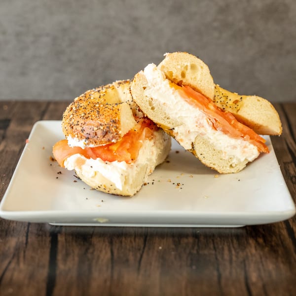 Everything bagel with cream cheese and lox, sliced in half on a white plate.