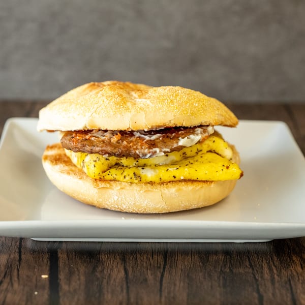 Breakfast sandwich with sausage patty, scrambled egg, and sauce on a toasted bun.