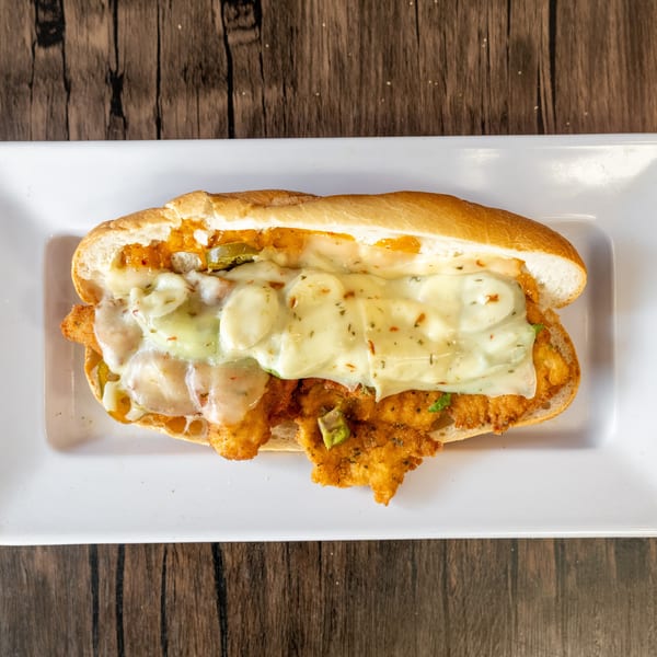 A crispy chicken sandwich with melted cheese and jalapeños on a white plate.