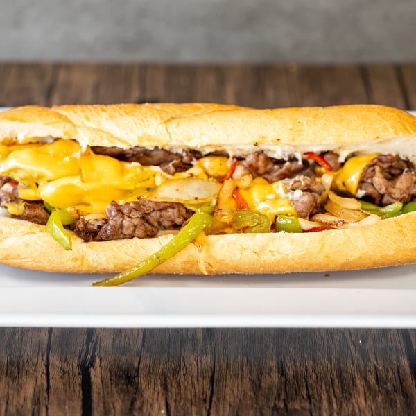 A delicious cheesesteak sandwich with melted cheese, steak, onions, and peppers on a white plate.