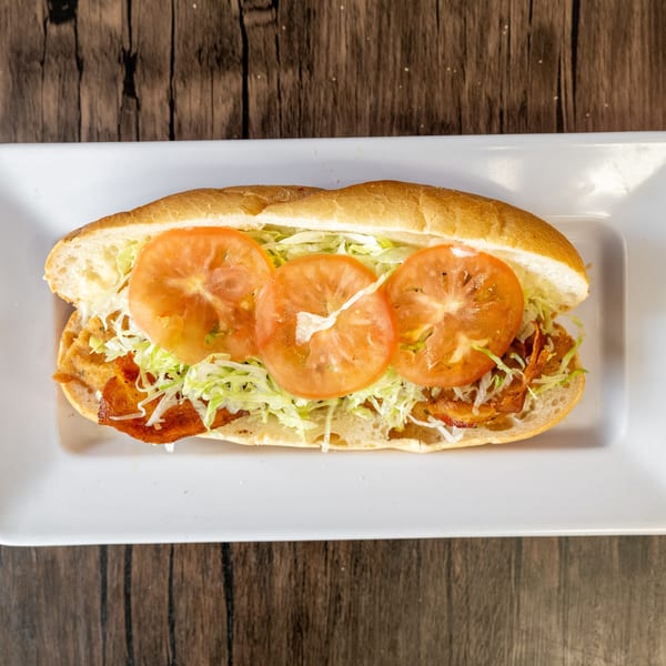 A bacon, lettuce, and tomato sandwich on a white rectangular plate, on a dark wooden table.