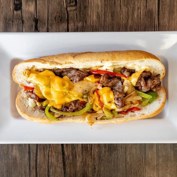 A delicious cheesesteak sandwich with melted cheese, steak, onions, and peppers on a white plate.
