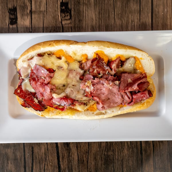 A close-up, overhead view of a hot pastrami and cheese sub sandwich on a white plate.