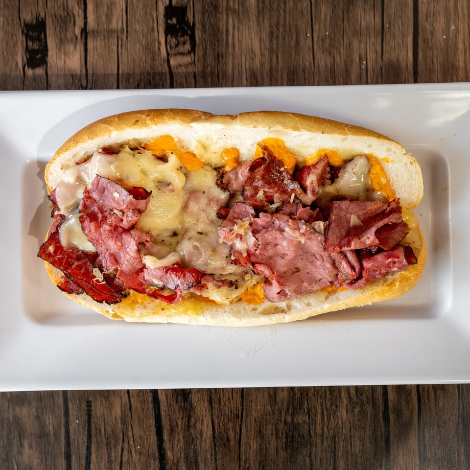 A close-up, overhead view of a hot pastrami and cheese sub sandwich on a white plate.