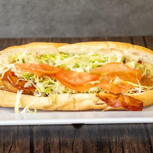A long sub sandwich filled with fried chicken, bacon, shredded lettuce, and sliced tomatoes.