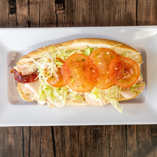 A turkey and bacon sub sandwich with lettuce and tomatoes on a white plate.