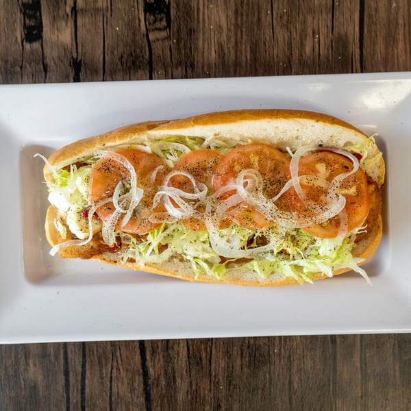 A submarine sandwich with lettuce, sliced tomatoes, and onions on a white rectangular plate.