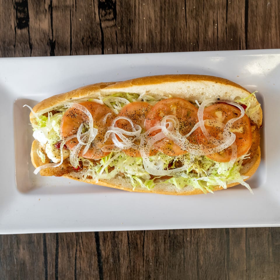 A long sub sandwich with lettuce, sliced tomatoes, and onions on a white plate.