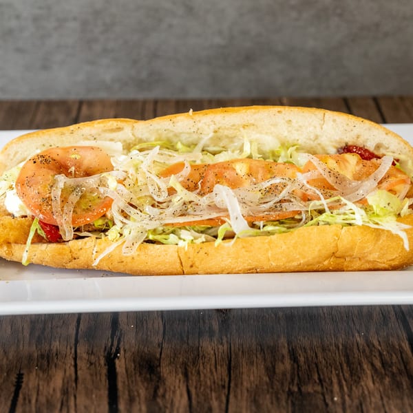 A long submarine sandwich filled with lettuce, tomatoes, onions, and sauce on a white plate.