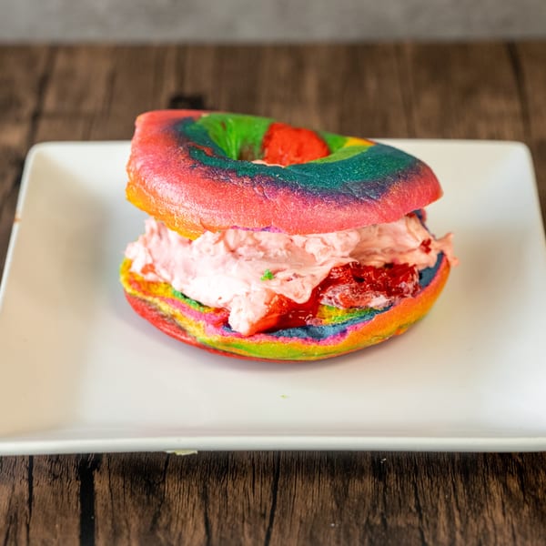 Rainbow bagel with strawberry cream cheese and jam on a white rectangular plate.