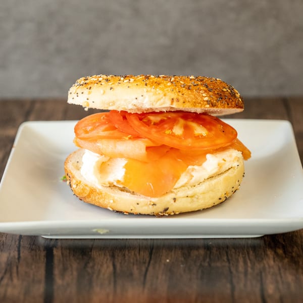 Everything bagel with cream cheese, smoked salmon, and sliced tomatoes on a white plate.